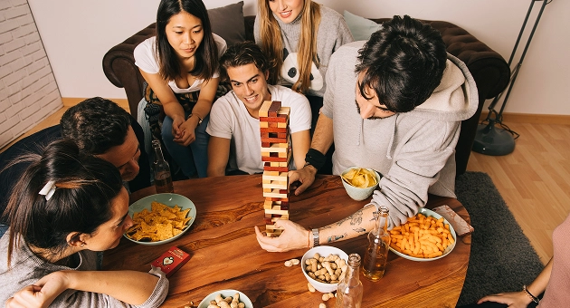 Een groep vrienden speelt Jenga aan een tafel met hapjes en drankjes